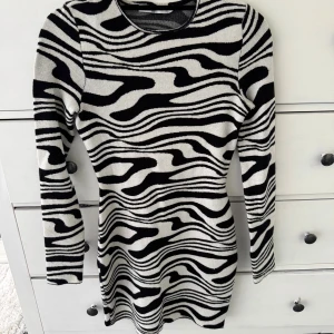 Zebramönstrad klänning från NA-KD - Snygg kort klänning från NA-KD med svartvitt zebramönster. Modellen har lång ärm, rund hals och en stor öppen rygg med snörning. Materialet är mjukt och stretchigt, vilket gör den bekväm och följsam. Perfekt för dig som gillar att sticka ut med coola detaljer.Bara använd en gång. 