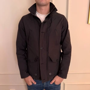 Safari jacka Tommy Hilfiger - Svart vindjacka från Tommy Hilfiger. Jackan har knappstängning framtill och är tillverkad i slitstark polyester. 