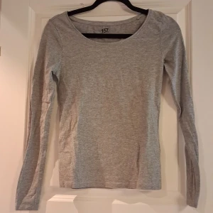 Grå långärmad topp från 157 - En enkel och stilren grå långärmad topp från 157. Modellen har rund halsringning och är figurnära i passformen. Perfekt att matcha med jeans eller kjol för en clean look. Materialet känns mjukt och bekvämt mot huden.