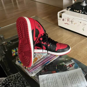 Nike Air Jordan 1 Bred Highs - Säljer ett par Nike Air Jordan 1 Highs i den klassiska Bred-färgen. Skorna har svart och rött skinn med vita detaljer på sulan, ikonisk Jordan-logga på sidan och tungan, samt snörning. Perfekt för dig som gillar streetstyle och sneakers med attityd. 
