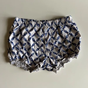 Blåvita shorts med fiskmönster H&M - Söta shorts från H&M i vitt med blått fiskmönster. Modellen är loose och har resår i midjan och vid bensluten för en bekväm passform. Tillverkade i mjuk bomull, perfekta för varma sommardagar.