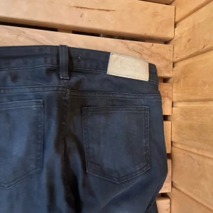 Mörkblå jeans från Acne Studios - Snygga mörkblå jeans från Acne Studios med klassisk femficksdesign och smal passform. Jeansen har gylf med dragkedja och knapp, samt diskret Acne-logga på bakfickan. Perfekta för dig som gillar stilrena och tidlösa jeans.