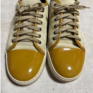 Lanvin sneakers med gul lackad tå - Lanvin sneakers i beige mocka med snörning och rund tå. Tåpartiet är i blankt gul lack och har vita gummisulor. Snygga kontraster mellan mocka och lackdetaljer, samt diskret Lanvin-logga på innersulan. Perfekt för dig som gillar unika designer.