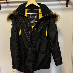 Svart parkajacka Alpha Industries M - Parkajacka från Alpha Industries i svart med gul quiltad insida. Väldigt varm med många fickor använd max 3 gånger. Storlek M 