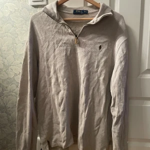 Beige half zip tröja från Polo Ralph Lauren - Snygg beige långärmad tröja från Polo Ralph Lauren med half zip och klassisk broderad logga på bröstet. Tillverkad i mjuk bomull och perfekt för lager-på-lager. Enkel och stilren design som funkar året runt.