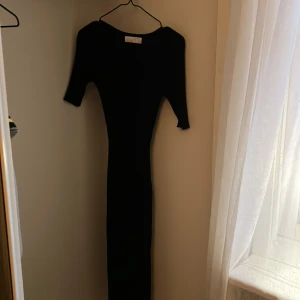 Svart långklänning från SAMSA Collection - Säljer en svart långklänning från SAMSA Collection i storlek XS. Klänningen har en figurnära passform med trekvartsärm och en stilren, minimalistisk design. Perfekt för dig som gillar klassiska och eleganta plagg.