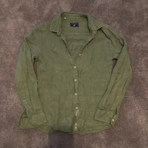 Grön linneskjorta från Polo horse - Snygg grön skjorta från Polo Horse i mjukt linne. Klassisk krage, långärmad och med knappar hela vägen framtill. Skjortan har en relaxed passform och är perfekt att bära över en t-shirt. Enkel och stilren design utan mönster.