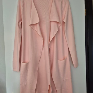 Ljusrosa cardigan jacka från Chica London - Mysig ljusrosa cardigan jacka från Chica London med lång ärm, öppen framtill och två stora fickor. Jackan är stickad i ett mjukt material och har en avslappnad passform med snyggt fall framtill. Perfekt för lager-på-lager och chill vibes. Är I nyskick och passar Medium-Large skulle jag säga.