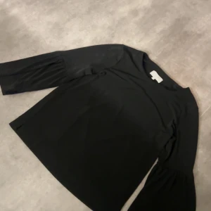 Svart blus med vida ärmar - Säljer en svart blus med rund hals och snygga vida trekvartsärmar som har lätt rynk vid axeln. Toppen har en stilren och enkel design. Materialet känns mjukt och har en lätt stretch. 