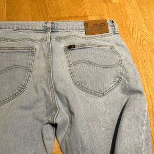 Ljusblå jeans från Lee - Säljer ett par klassiska ljusblå jeans från Lee med raka ben och femficksmodell. Jeansen har Lee-logga på bakfickan och läderpatch i midjan. Tillverkade i slitstarkt bomullsjeans, perfekta för en avslappnad och tidlös look.