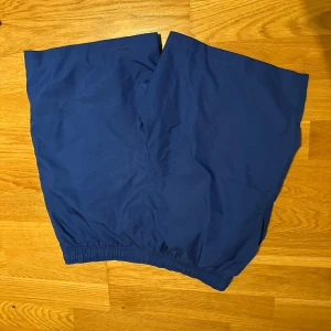 Blå Lacoste Sport shorts med resår - Säljer ett par blå sportiga shorts från Lacoste Sport med elastisk midja och klassisk krokodillogga på sidan. Modellen är loose fit och har enkel design utan mönster, perfekta för träning eller chill. Materialet är polyester och de är riktigt sköna att bära.