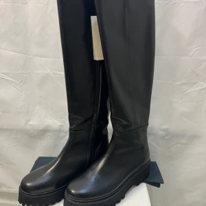 Stövlar str 40,5 från Dorothee Schumacher 100% skinn  - Snygga svarta höga stövlar från  Dorothee Schumacher i storlek 40,5 Inköpta på www.MyTheresa.com. Nypris 5000 kr. Stövlarna har en clean och modern look med rund tå, platt sula och grovt mönstrad yttersula. Tillverkade i slätt skinn med dragkedja på insidan för enkel påtagning. Perfekt för dig som gillar stilrena boots.