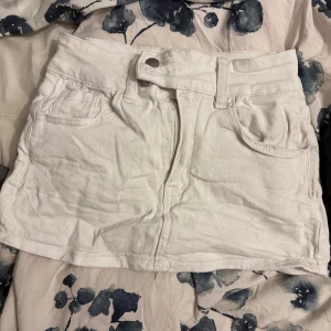 Vit jeanskjol med fickor - Snygg vit kort jeanskjol med klassisk femficksdesign och bälteshällor. Kjolen har knapp och dragkedja framtill samt två bakfickor. Perfekt för dig som gillar en enkel och stilren look.