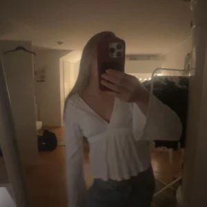 Vit omlottblus med knyt i midjan - Säljer en vit omlottblus med v-ringning och långa, lite utsvängda ärmar. Blusen har ett snyggt knyt i midjan som ger en feminin siluett och är lätt att styla till jeans eller kjol. Materialet känns mjukt och luftigt, perfekt för vår och sommar.