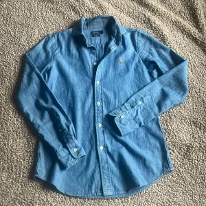 Blå skjorta från Polo Ralph Lauren - Snygg blå skjorta från Polo Ralph Lauren i en slim custom fit. Skjortan har klassisk krage, långa ärmar och knäppning framtill. Ikoniska broderade polospelaren på bröstet. Perfekt för dig som gillar stilren och tidlös design. Storlek S. Inga defekter nästan helt ny. NYpris: 2200kr MITT pris: 499kr🤪Har du frågor kring skjortan? Skriv så svarar jag så snabbt som möjligt! MVH SWISSWEAR🇨🇭🍾🏔️