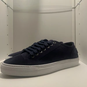 Mörkblå sneakers från Brioni - Brioni Suede sneakers i mörkblått är en exklusiv sneaker från Brioni i mocka med stilren vit sula och en subtil Brioni-logga på häl och sula ger dig en sneaker som andas diskret lyx. För dig som uppskattar ren design och högsta kvalitet. dessa är helt nya, i box med dust bag. Nypris: 8500kr+ Vårt pris: 4350kr