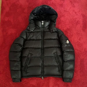 Svart Moncler dunjacka med huva - Intressekoll på min Moncler Maya (priset jag satt är då ungefär vad jag vill ha för den, så kom med bud!). Den är perfekt för vintern med sitt quiltade mönster och långa ärmar. Jackan har en dragkedja framtill och en huva för extra skydd mot kylan. Den är i nyskick och kommer med originalpåse. Den har både NFC scan och QR scan🖤 