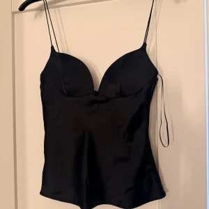 Svart satinlinnetopp från Zara - Aldrig använd!🥰 Supersnygg svart linne-topp från Zara i satinliknande material. Toppen har tunna axelband, formade kupor och en smickrande passform. Dragkedja i sidan för enkel påklädning. Perfekt för att lyfta vilken outfit som helst.