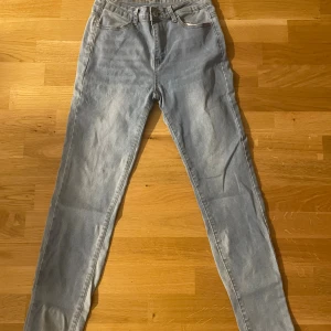 Ljusblå skinny jeans med hög midja - Säljer ett par ljusblå skinny jeans med klassisk femficksdesign och hög midja. Jeansen har bälteshällor, dragkedja och knapp framtill. Perfekta för dig som gillar en tight passform och vill ha en enkel, stilren look.