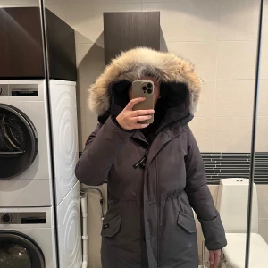 Grå Canada Goose parkas med päls - Säljer en grå parkas från Canada Goose med stor fluffig päls på huvan och klassisk logga på ärmen. Jackan har dragkedja, snörning i midjan och praktiska fickor. Perfekt för kalla vinterdagar och riktigt snygg siluett. Box ingår samt ett jacköverdrag. Pälsen går även att ta av. Köpte jackan för 4 år sen för ungefär 12 000. Den har även kemtvättats och är ren.