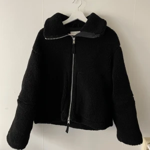 Teddyjacka - Säljer denna svarta teddyjackan från hm. Använt den då och då i två vintrar, men fortfarande i fint skick! Jättemysig på vintern och har en hög hals som också går att vika ner om man vill🥰. Nypris 600kr, säljer för 400kr!💕