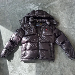 Svart pufferjacka från Polo Ralph Lauren - Glansig Ralph Lauren jacka i toppskick! Stilren, varm och perfekt för vintern som står runt hörnet. Passar både till vardag och skola. ✅️❄️                                                                                                                                Hör av dig vid minsta lilla fråga!
