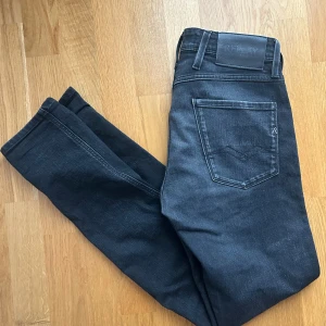 Replay Anbass svarta slim jeans - Snygga svarta Replay Anbass jeans i slim fit med klassisk femficksdesign och diskreta slitningar. Jeansen har en mörk tvätt och är tillverkade i stretchigt denim för en bekväm passform. Perfekta för dig som gillar en stilren look. 28/32