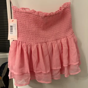 Rosa volang tubtopp från Nelly - Supersöt rosa tubtopp från Nelly med smockad överdel och dubbla volanger nedtill. Denna tröjan är i storlek M och är inte använd. Passar perfekt som topp men också som kjol.❣️