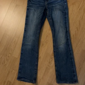 Blå jeans med raka ben och fickdetaljer - Snygga blå jeans från Gina tricot med but cut ben och coola fickor bak med lock och knapp. Jeansen har klassisk femficksdesign, dragkedja och knapp framtill samt slitningar för en avslappnad look. Perfekt för dig som gillar streetstyle. STORLEK 164!!!