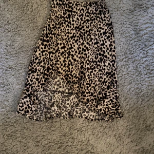 Leopardmönstrad kjol med volang - Säljer en snygg leopardmönstrad kjol med volangkant nertill. Kjolen har en beige och svart färgskala och är i en mjuk, lätt polyester. Modellen är något längre bak än fram och har en skön passform i midjan.