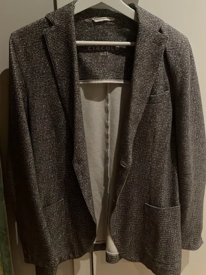 Grå rutig kavaj från Circolo 1901 S/M - Snygg grå kavaj från Circolo 1901 med diskret rutigt mönster och klassisk krage. Kavajen har två framfickor och är helfodrad med ljus insida. Perfekt för dig som gillar stilrena och moderna plagg med en twist. Mitt pris 1049kr