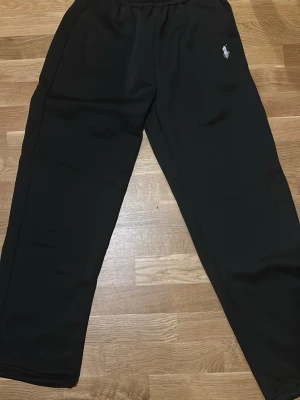 Svarta mjukisbyxor från Polo Ralph Lauren - Svarta mjukisbyxor från Polo Ralph Lauren med klassisk vit broderad logga på benet. Byxorna har elastisk midja och är tillverkade i mjukt material som känns skönt mot huden. Perfekta för chill dagar eller när du vill ha en clean look. Pris kan diskuteras.