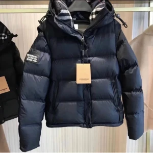 Svart pufferjacka från Burberry - Svart pufferjacka från Burberry med avtagbar huva och klassiskt rutigt foder. Jackan har dragkedja och knappar framtill, samt två sidofickor med dragkedja. Patch med Burberry London England på ärmen. Perfekt för kalla dagar.