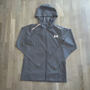 Under armour windbreaker jacka storlek L/M - Snygg grå windbreaker från Under armour som även går att använda som zip hoodie. Jackan har reflekterande detaljer, logga på bröstet och är väldigt lätt. Storleken är L, men är något mindre i storleken så passar nog M också.