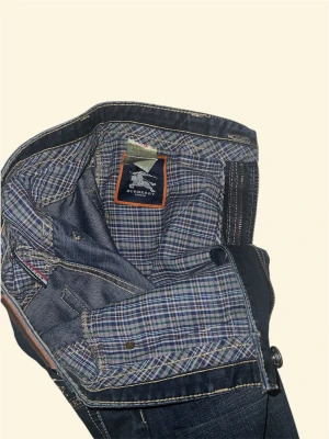 Burberry mörkblå  jeans - Snygga mörkblå jeans från Burberry med kontrastsömmar. Insidan har rutigt tyg med Burberry London-logga. Jeansen har fem fickor och dragkedja fram. Perfekt för dig som gillar stilrena detaljer och premiumkänsla.