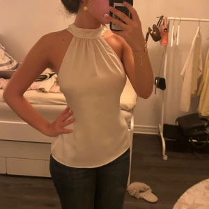 Figursydd Blus - Säljer en stilren vit/champagne färgad halterneck linnetopp. Den har dragkedja där bak. Jag har sytt in den hos skräddare för att få en mer fogurnära passform. Toppen är satin, med glansig yta. Nu har jag inte strykt den på bilden, men den är finare då. Använt några gånger. Kontakta för fler bilder o info ❤️