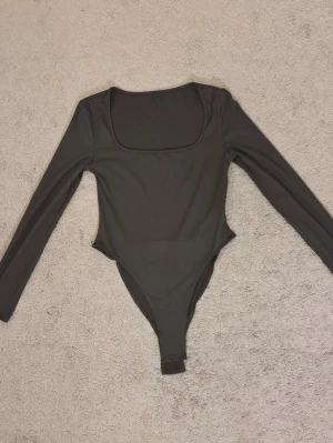 Grå långärmad body - Säljer en helt vanlig mörkgrå bodysuit, långärmad. Materialet är skönt och den sitter fint. Passar till vad som!