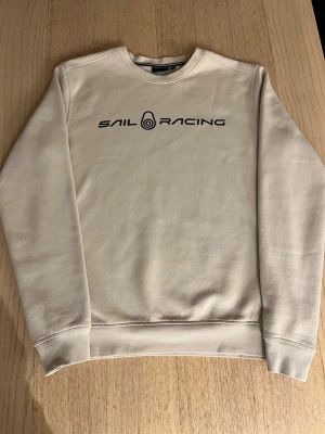 Beige Sail Racing sweatshirt  - Beige Sail Racing sweatshirt med tryck på bröstet, storlek S men kan passa någon med M, ny pris ca 900kr.   Minimal fläck på vänster armen, se sista bilden. Tveka inte att höra av dig vid minsta fundering