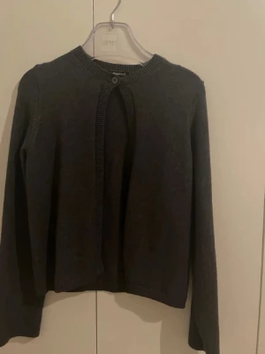 Mörkgrå kofta från Gina - Snygg mörkgrå kofta från gina med rund hals och en knapp framtill. Koftan är stickad i mjukt material och har långa ärmar. Perfekt att slänga över en t-shirt eller linne för en chill look.