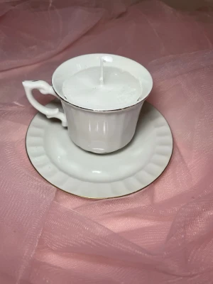 Doftljus i en tekopp i en vit färg nr 2  - Det här ljuset är gjort av återanvändbara material. Tekoppen är köpt secondhand och stearinet är från kyrkor som tänkte slänga det. Det här ljuset har en svag doft utav vanilj, så känsliga även kan använda det. Det finns även fler ljus med denna design på hemsidan, om man vill köpa sets. 