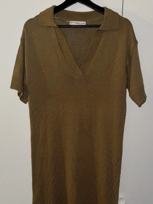 Beige stickad klänning från MNG - Stickad beige klänning från MNG i storlek XS. Modellen har korta ärmar, v-ringad hals med krage och är i en loose passform. Materialet är mjukt stickat och klänningen har en enkel, stilren design utan mönster eller extra detaljer.