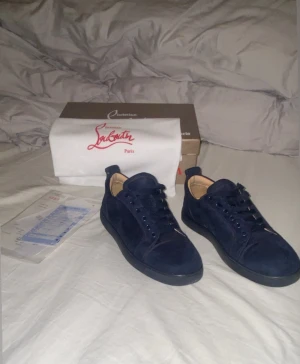 Mörkblå mocka sneakers Christian Louboutin - Snygga mörkblå sneakers från Christian Louboutin i mjuk mocka med klassisk röd signatursula. Storlek 41 sitter som 41,5 / 42. Skorna är i dunder skick förutom en liten skavank, som ni ser på bild 3 är ringen borta men inget som märks eller syns på avstånd! Skorna kommer med tags och allt annat även box! Hör av dig vid minsta fundering 🤩