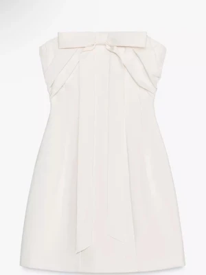 Vit axelbandslös kortklänning med rosett - Supersnygg vit axelbandslös kortklänning från Zara med stor rosettdetalj framtill. Klänningen har en elegant och stilren design med raka linjer och lätt A-linjeformad siluett. Perfekt för dig som vill sticka ut med en chic och modern look. Köpte till studenten men är inte säker på om ja vill ha den längre vill därför se vad jag kan få för den💕