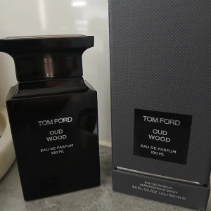 Tom Ford Oud Wood EdP 100ml - Tom Ford Oud Wood Eau de Parfum 100 ml i lyxig, mörkbrun fyrkantig glasflaska med svart etikett och matchande kartong. Flaskan har en elegant och modern design med tydliga linjer och exklusiv känsla. Perfekt för dig som gillar träiga och sofistikerade dofter.
