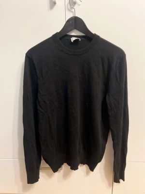 Svart stickad tröja från Filippa K - Svart stickad tröja från Filippa K i storlek M. Klassisk rund halsringning och långa ärmar. Tröjan är tillverkad i mjuk ull och har ribbade muddar vid ärmslut och nederkant. Perfekt för dig som gillar stilrena och enkla plagg.