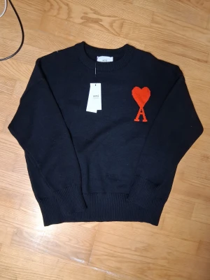 Ami Paris tröja - Svart stickad tröja från Ami. På bröstet finns ett rött hjärta med bokstaven A, som ger en unik och snygg detalj. Materialet är mjukt och skönt. Den är knappt använd så ny skick med inga tecken på användning. Köpt av min vän på miinto.se men tyvärr passar den inte han. Man får med påsen som den kom in.