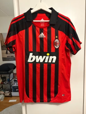 AC Milan fotbollströja Ronaldo 99 - Säljer en klassisk AC Milan fotbollströja från Adidas med Ronaldo och nummer 99 på ryggen. Tröjan har röd och svart randigt mönster, vit logga och klubbmärke på bröstet. Perfekt för dig som älskar fotboll och retrostil.