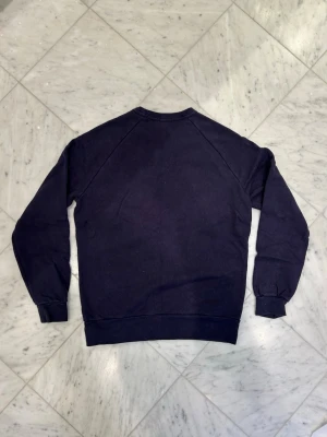 Mörkblå sweatshirt med rund hals - En enkel och stilren mörkblå sweatshirt med rund hals och långa ärmar. Tröjan har ribbade muddar vid ärmslut och nederkant, vilket ger en skön passform. Perfekt för chill dagar eller när du vill ha en clean look.