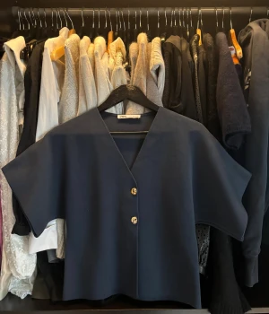 Mörkblå blus med guldknappar från Zara - Säljer en stilren mörkblå blus från Zara med två snygga guldknappar framtill. Blusen har v-ringad hals, korta ärmar. 