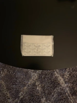 Vit plånbok - Säljer en stilren vit kuvertväska  det klassiska geometriska mönstret på framsidan. Väskan har en rektangulär form och är tillverkad i skinn med snygga detaljer. Perfekt för dig som gillar minimalistisk design och vill ha något unikt.